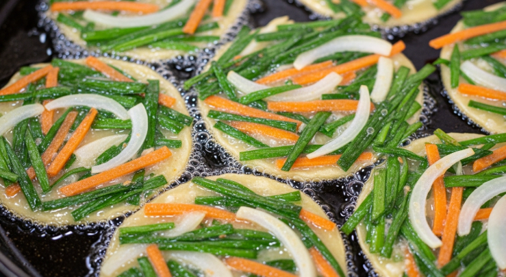 지글지글 기름 위에서 부추전이 얇게 펴져 가장자리가 갈색으로 바삭하게 익어가는 모습.