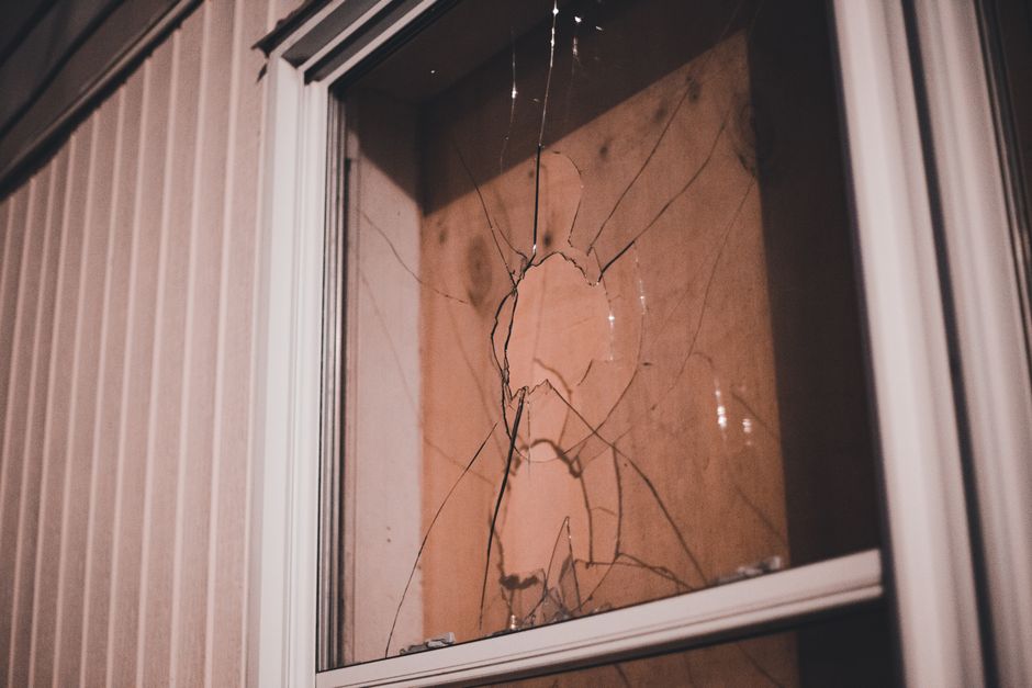 Detailed view of a cracked window pane at night, highlighting textures and reflections.
