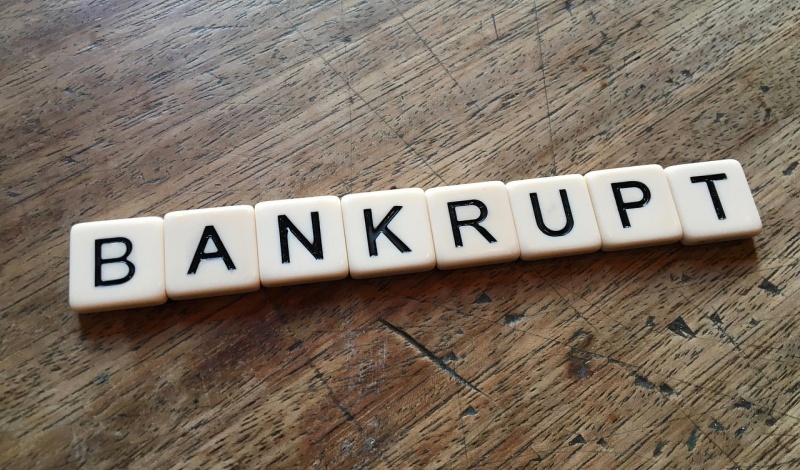 Word BANKRUPT spelled out with tiles on a wooden table symbolizing financial distress