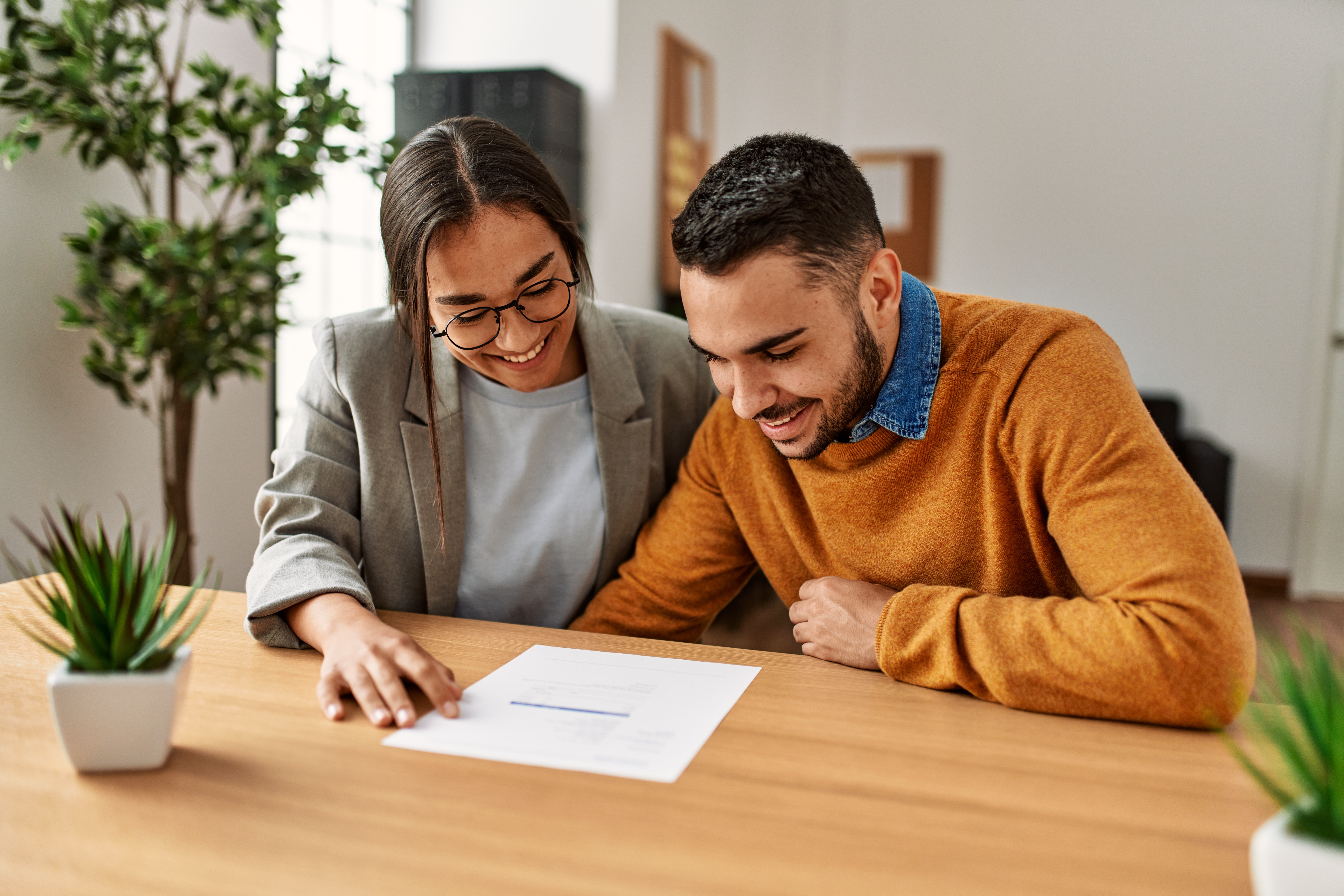 청년 남녀가 임대차 계약서 또는 신청 서류를 함께 검토하며 웃고 있는 모습