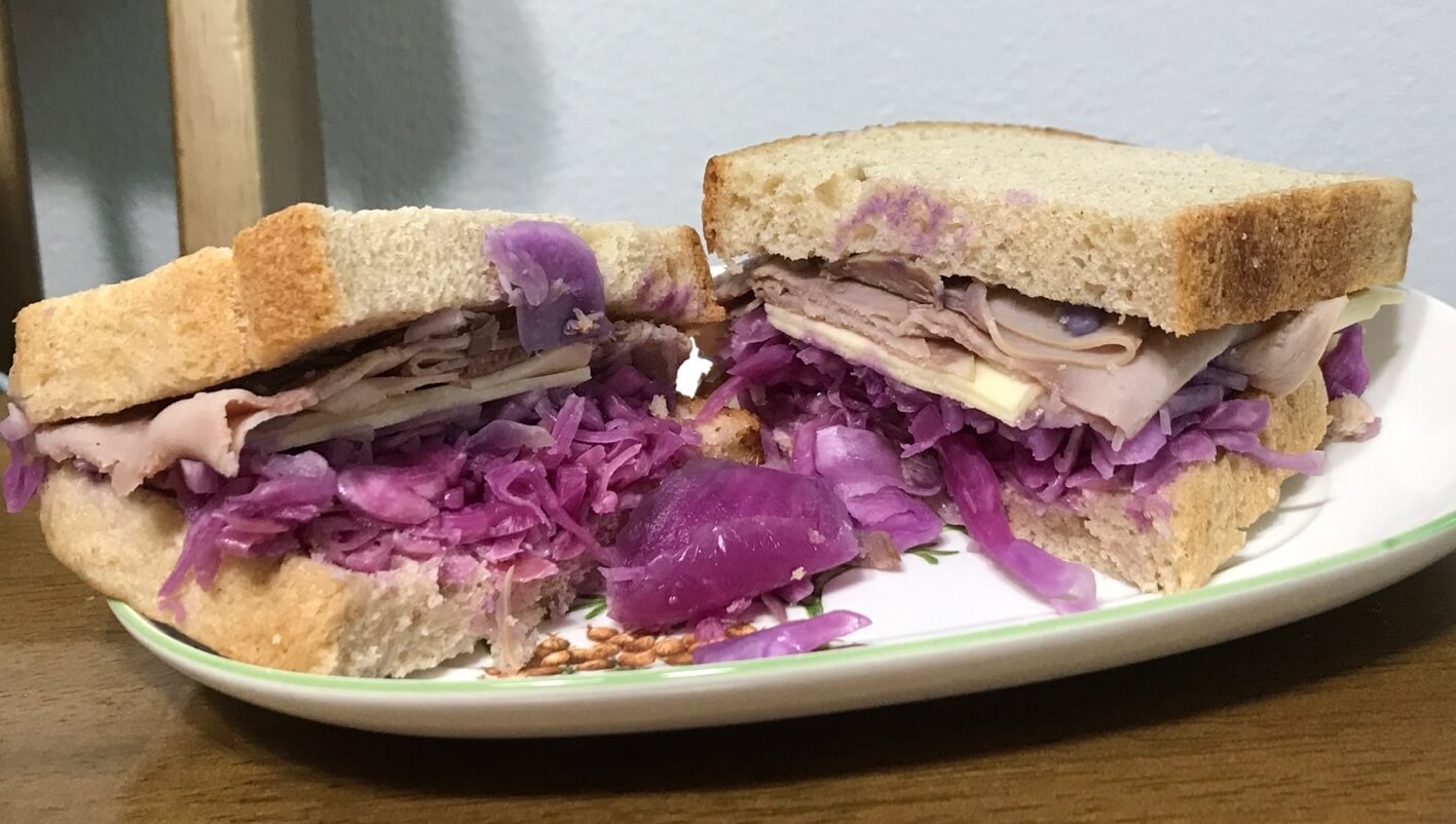 스타벅스 파스트라미 햄 치즈 샌드위치를 반으로 자른 모습입니다. 보라색 양배추, 파스트라미 햄, 치즈가 들어있습니다.