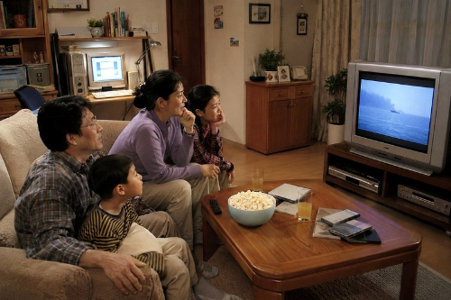 가족이 거실 소파와 바닥에 함께 앉아 브라운관 TV로 영화를 보는 모습