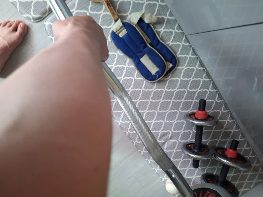 거실 매트 위에 놓인 EZ컬바, 조립식 덤벨, 아령, 악력기, 탁구채 등 다양한 운동기구.