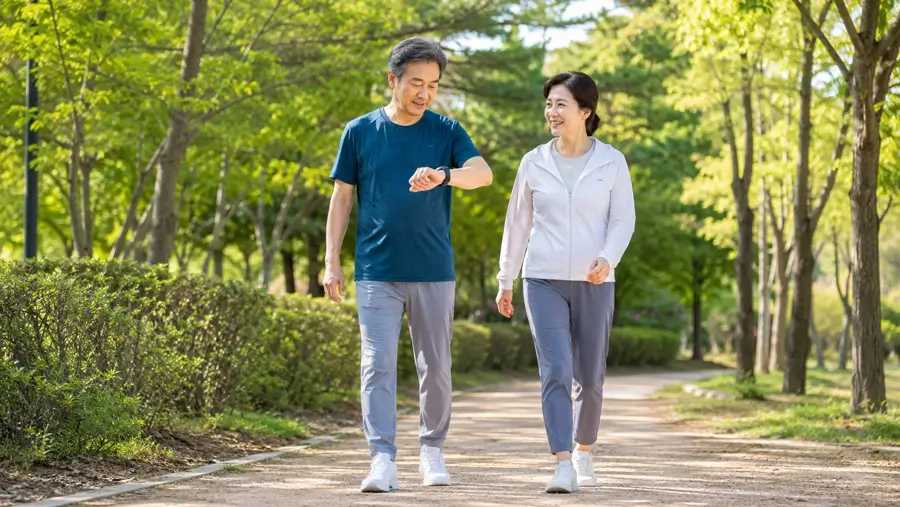 공원 산책로에서 편안한 운동복과 운동화를 착용하고 가볍게 걷는 한국인 중년 남녀, 한 사람은 손목 운동 기록을 확인하는 모습