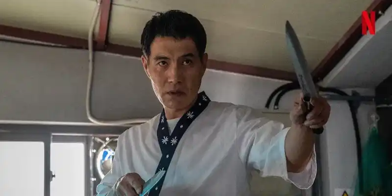 한 조립식 건물 안에서 요리복을 입고 두손에는 각각 칼을 들고 어느 누군가를 노려보면서 공격자세를 취하는 양중