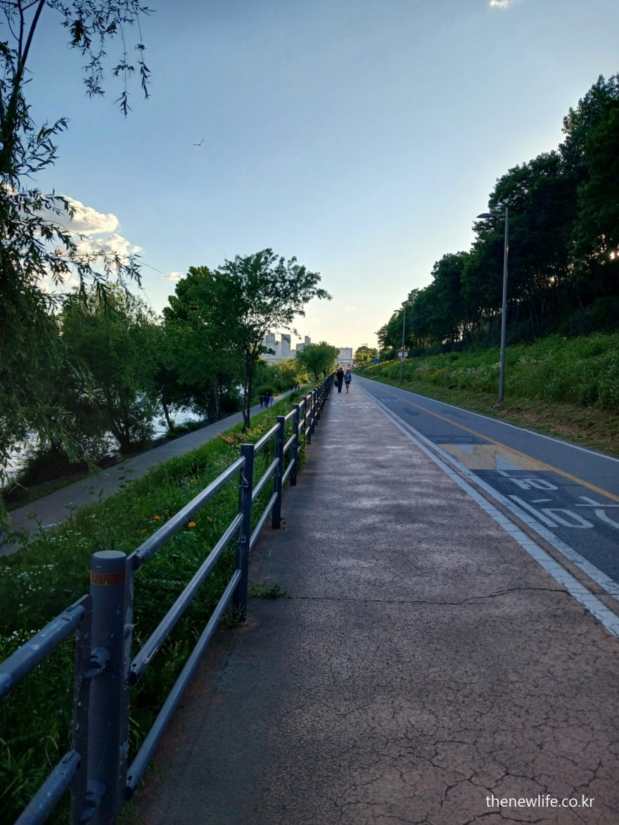 A peaceful bike and walking path just before sunset, with a clear sky and distant walkers. The image evokes a sense of calm and determination for health and exercise.-해 지기 직전의 고요한 자전거길과 산책로, 멀리 보이는 사람들과 맑은 하늘이 건강과 운동의 의미를 전합니다.