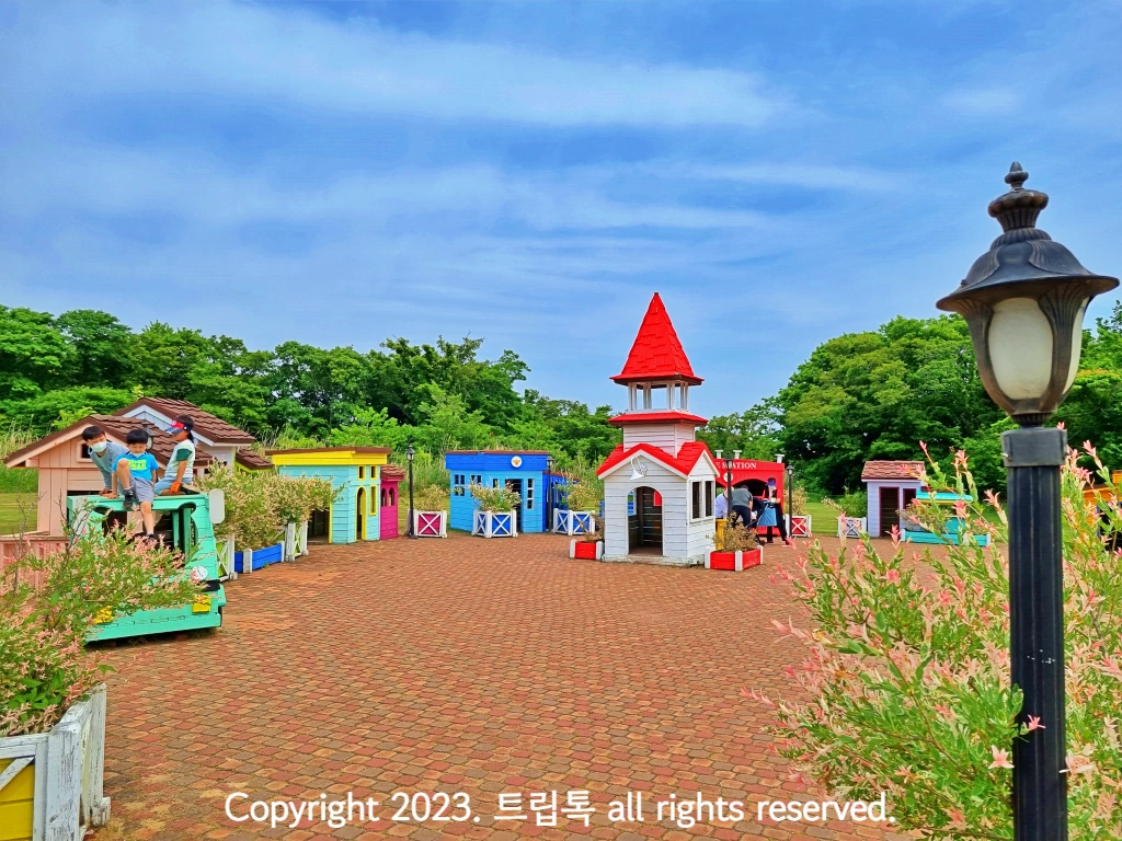 검정 가로등이 왼쪽에 있고 그 둘레에 나무로 만든 집이 있다.