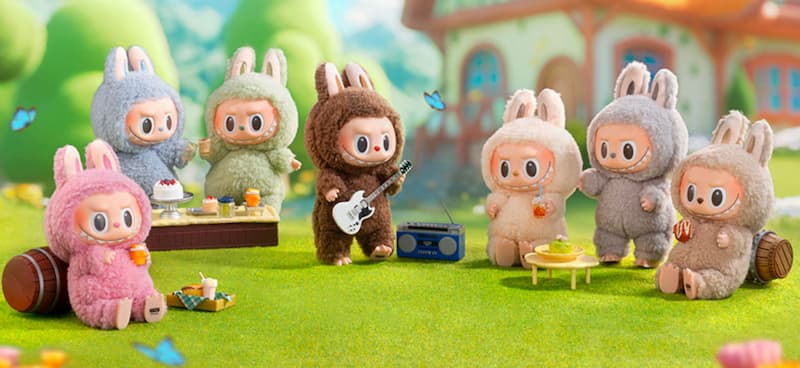 팝마트 인기 캐릭터 라부부 인형들이 야외 잔디밭에서 피크닉을 즐기며 기타를 연주하고 음료와 디저트를 나누는 장면. 귀여운 동화풍 배경과 캐릭터들이 조화를 이루고 있다.