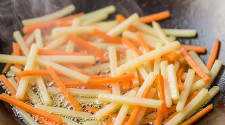 불에 감자채와 당근을 넣고 기름에 빠르게 볶고 있는 모습