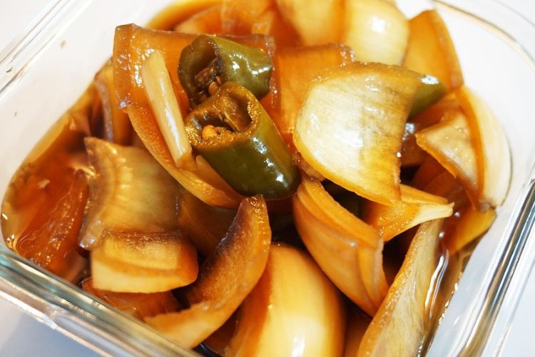 투명한 유리병에 아삭하게 썬 양파와 청양고추가 황금빛 절임액에 예쁘게 담겨있는 모습. 옆에는 물, 간장, 식초가 2:1:1 비율로 계량컵에 담겨있고, 배경에는 신선한 양파들이 자연스럽게 배치된 깔끔한 주방 환경. 따뜻한 자연광이 비치는 밝고 깨끗한 느낌의 요리 사진.