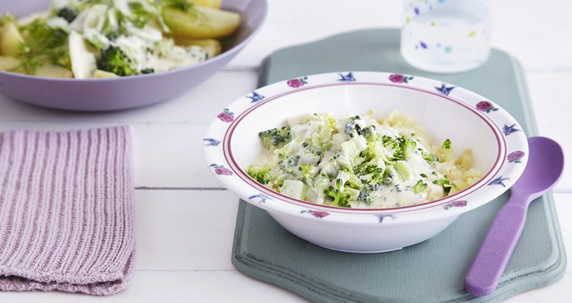 흰색 테이블 위에 흰 접시가 올라가 있고, 그 접시안에 초록색 야채(브로콜리)와 다른 음식들이 들어가 있다. 접시 옆으로는 보라색 스푼이 올라가 있다.