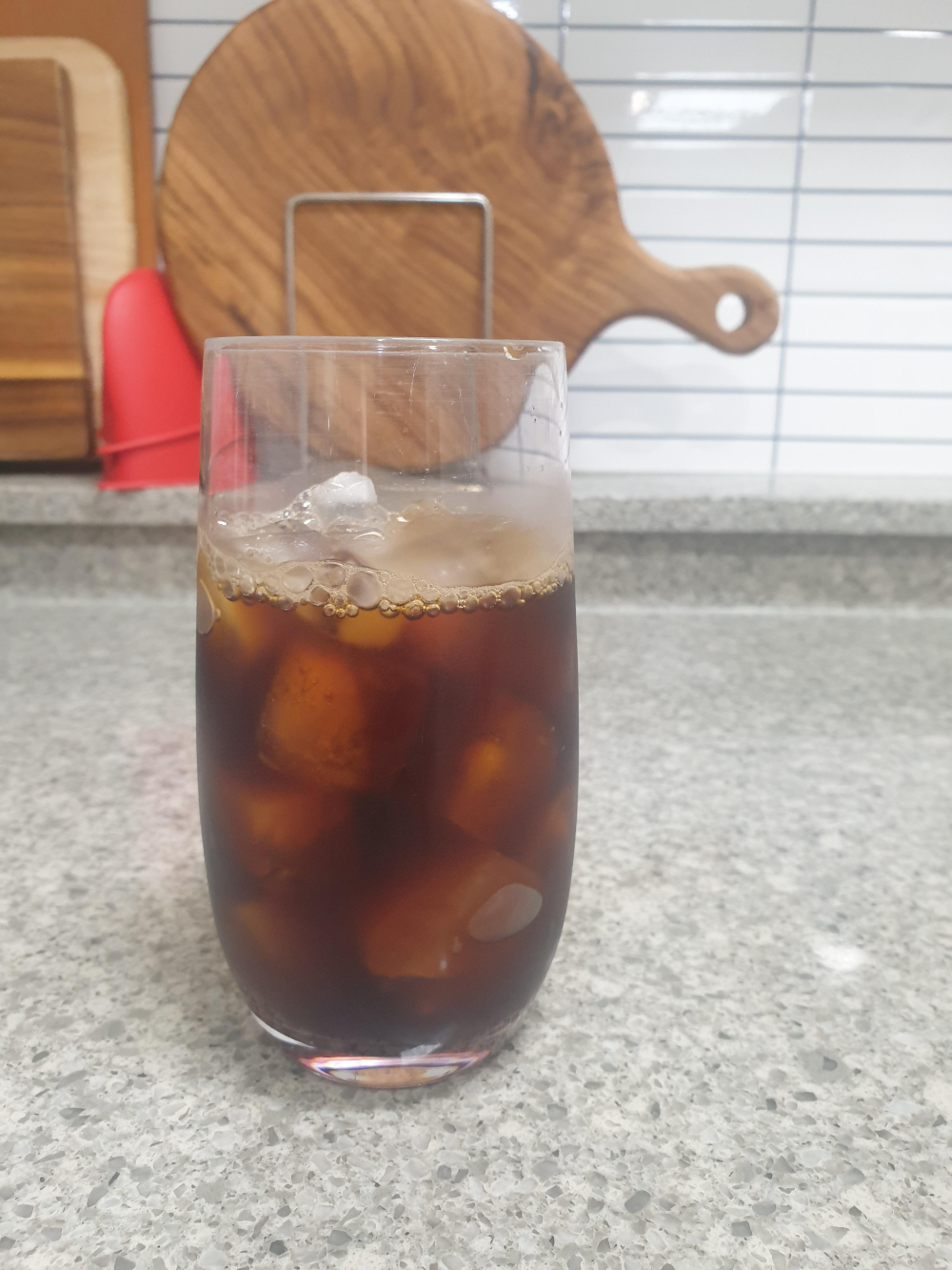 대리석 테이블 위애 추출된 아이스커피가 올려져 있다. 뒤쪽엔 도마가 보인다.