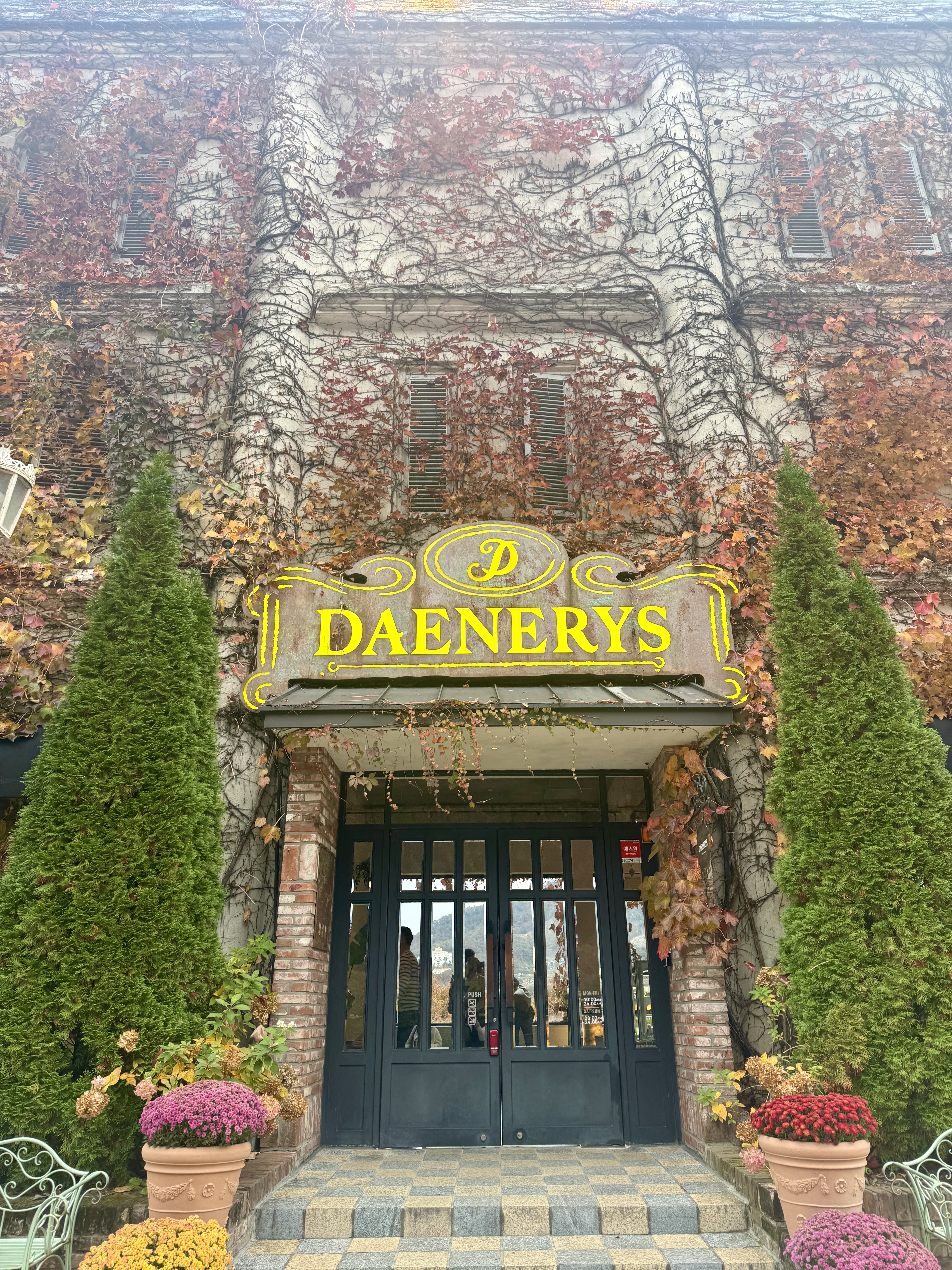 남양주 카페 데너리스 외관 모습. 담쟁이덩굴이 가득 덮인 건물과 노란색 DAENERYS 간판이 있는 입구