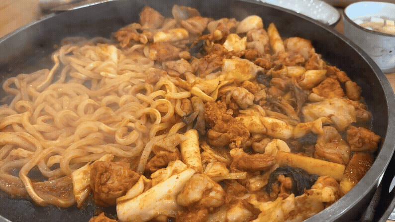 철판 위에 닭갈비와 우동사리가 완전히 익어 김이 모락모락 올라오고 있는 모습. 곧 젓가락이 닿을 듯한 먹기 직전 상태.