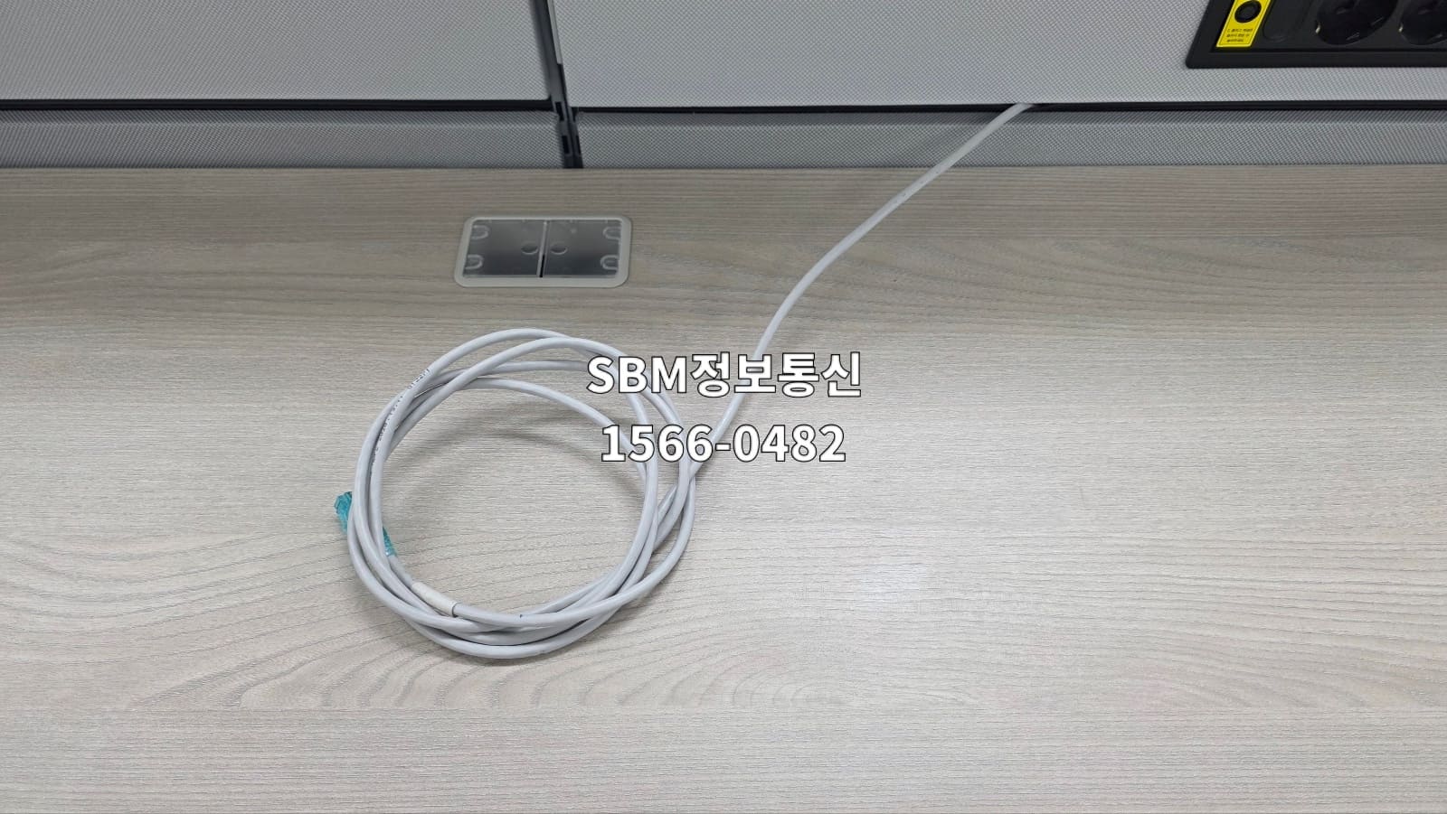 파티션 하부 틈을 통해 책상 위로 올라온 흰색 랜선 끝에 파란색 RJ45 커넥터가 연결된 모습
