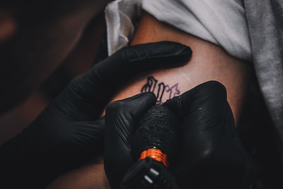 Detailed view of a tattoo artist crafting a tattoo design on skin with gloved hands.