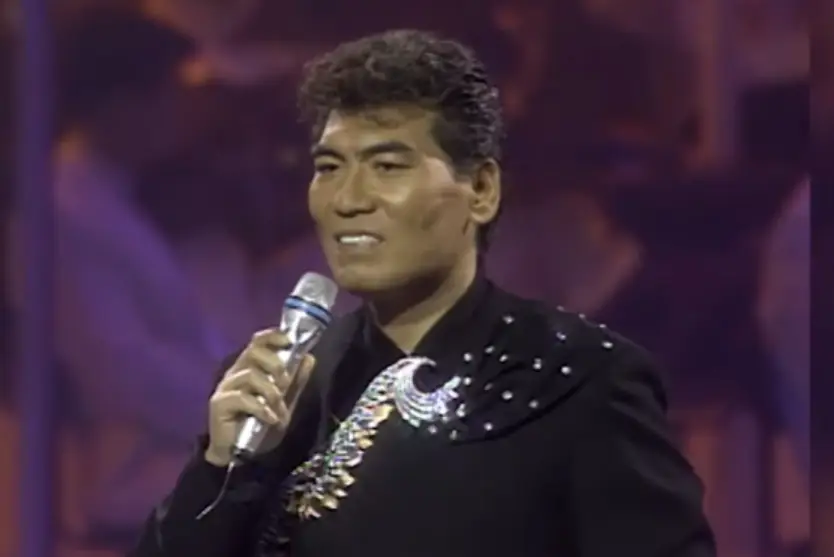 나훈아- 보라색 무대배경 검은 옷을 입고 오른손에 은색 마이크를 들고 노래하는 나훈아