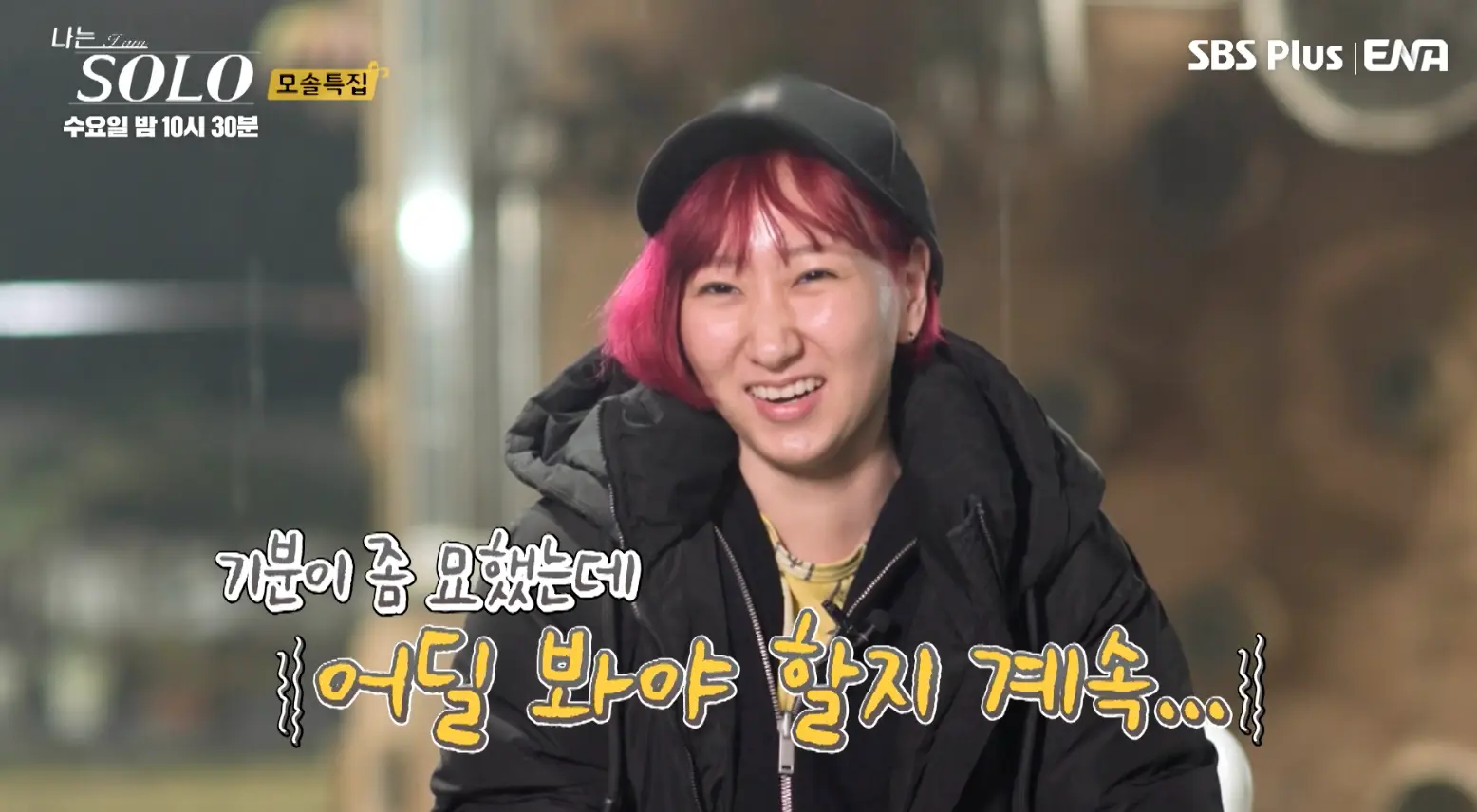 솔로- 붉은 머리 검은 챙모자를 쓰고 검은 쟈켓을 입고 흰의자에 앉아 인터뷰하는 영자