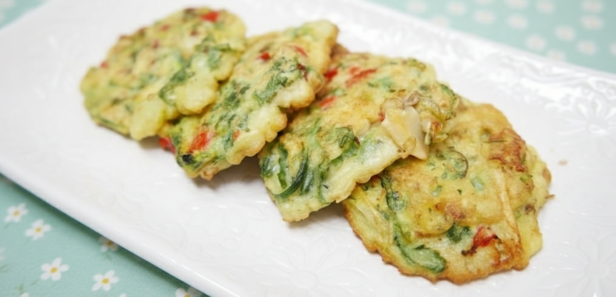 민트색 꽃무늬 식탁보 위에 놓인 노릇하게 부쳐진 냉이바지락전