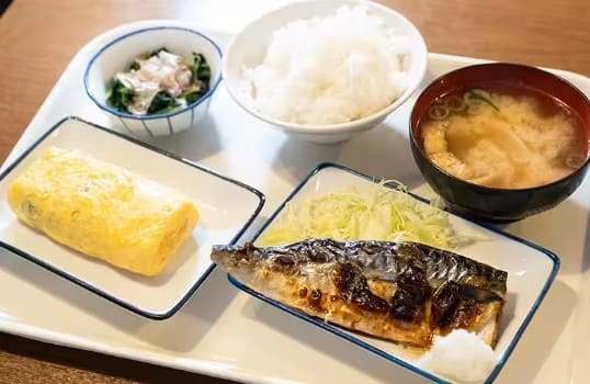 테이블위에 계란말이. 생선구이. 국. 밥등이 깔끔한 느낌으로 올라가 있다.