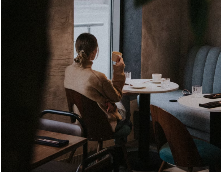 조용한 카페에서 창밖을 바라보며 커피를 마시는 여성. 주변에는 디지털 기기 없이 차분한 분위기가 흐르고 있다.