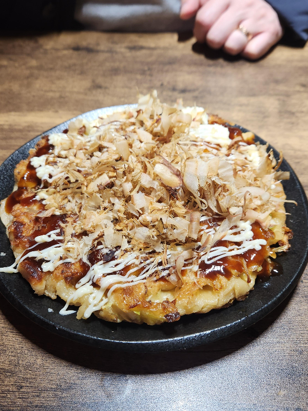 오코노미야끼 위에 소스와 가쓰오부시가 올려져 있다.