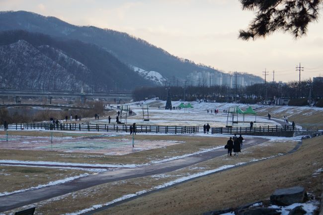 눈이 많이 녹은 청석공원 전경, 뒤로는 눈 쌓여 보이는 야사느 흐린 하늘, 공원에 보이는 여러 사람들,