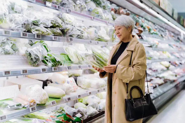 마트 채소 코너에서 포장된 신선한 채소를 고르고 있는 중년 한국 여성