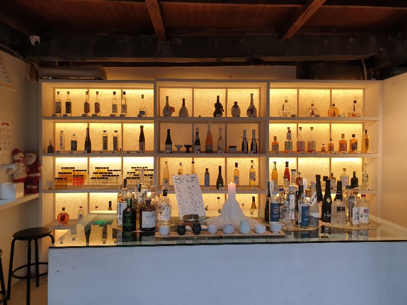 노란 조명을 뒤에 두고 진열되어 있는 술병, 앞에는 아일랜드에 술병들이 놓여 있다.