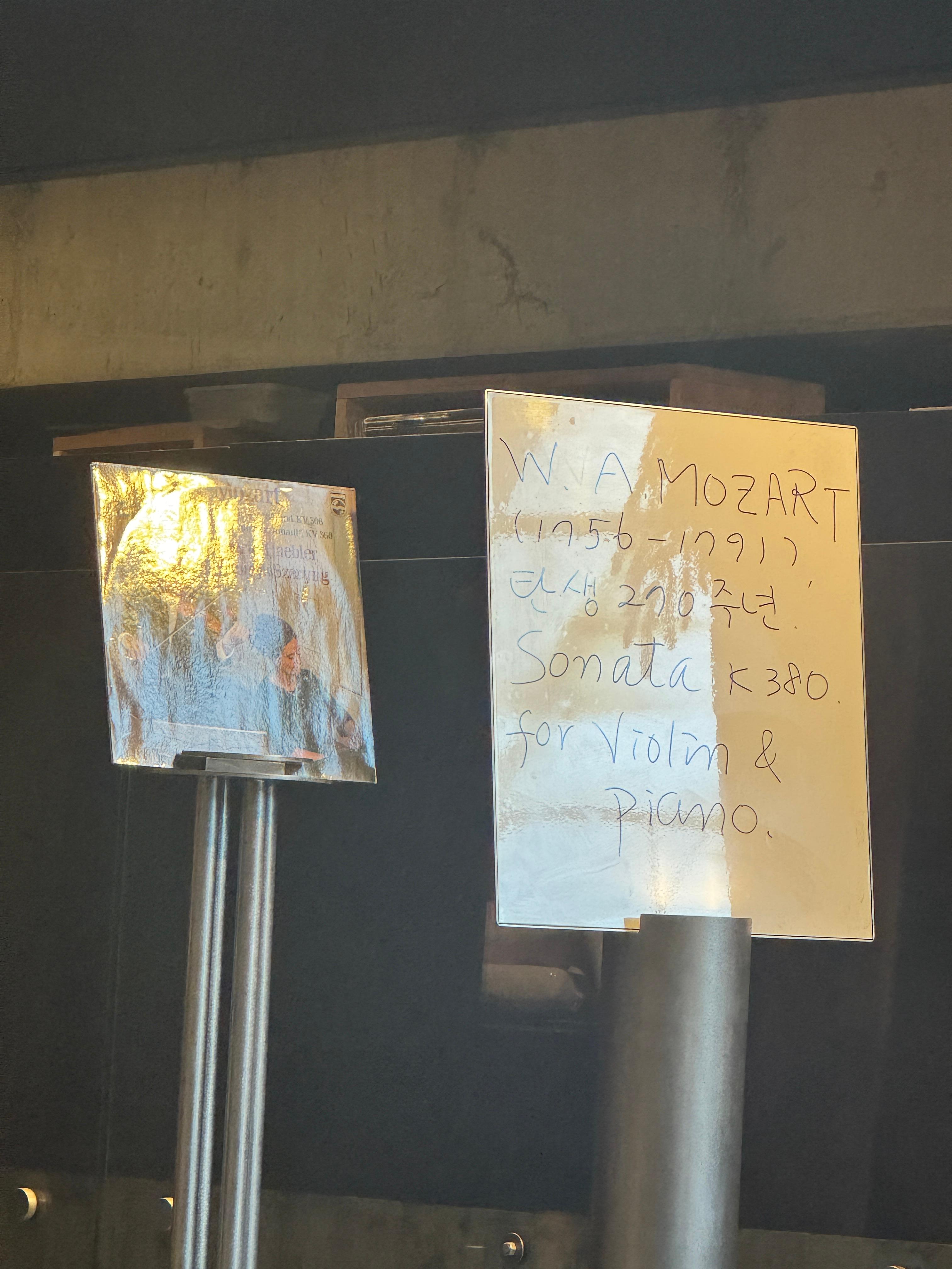 파주 헤이리 황인용 뮤직 스페이스 카메라타에서 현재 재생 중인 음악 안내판, 모차르트 바이올린 소나타 정보가 손글씨로 적힌 모습