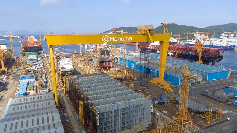 거대한 노란색 골리앗 크레인이 설치된 조선소 전경. 크레인에는 'Hanwha' 로고가 선명하게 새겨져 있으며, 드라이 도크 안에는 건조 중인 대형 선박 블록들이 배치되어 있다. 주변에는 수많은 장비와 야드 시설이 펼쳐져 있는 광활한 산업 현장의 모습이다.