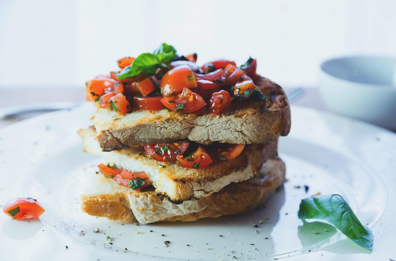 토스트 위에 토마토와 푸른잎 채소가 올라간 건강식이 접시에 담겨있다