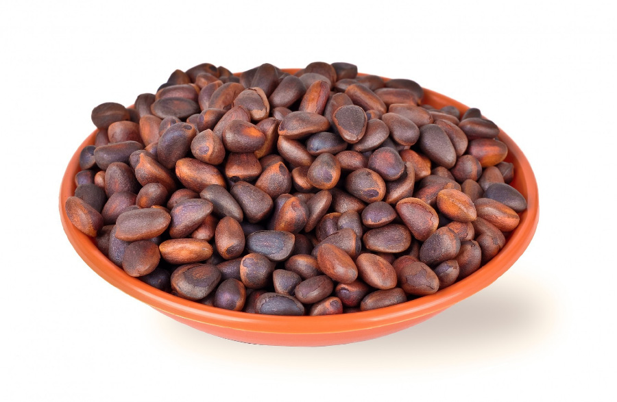 야생에서 채취를 한 껍질을 까지 않은 잣을 하얀 바닥 위에 동그랗고 고동색인 그릇에 가득 담아두고 찍은 사진