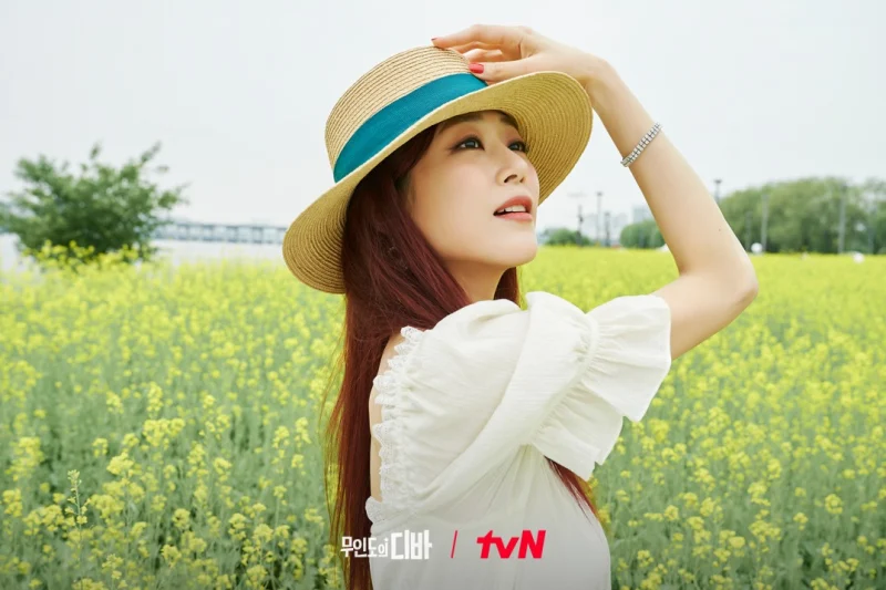 노란 꽃밭을 배경으로 흰 원피스를 입고 있는 무인도의 디바 윤란주 캐릭터