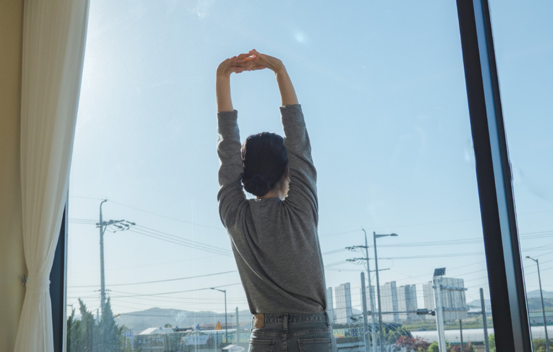 한 여성의 뒷모습이 팔을 높이 들며 피로를 풀고 있다.