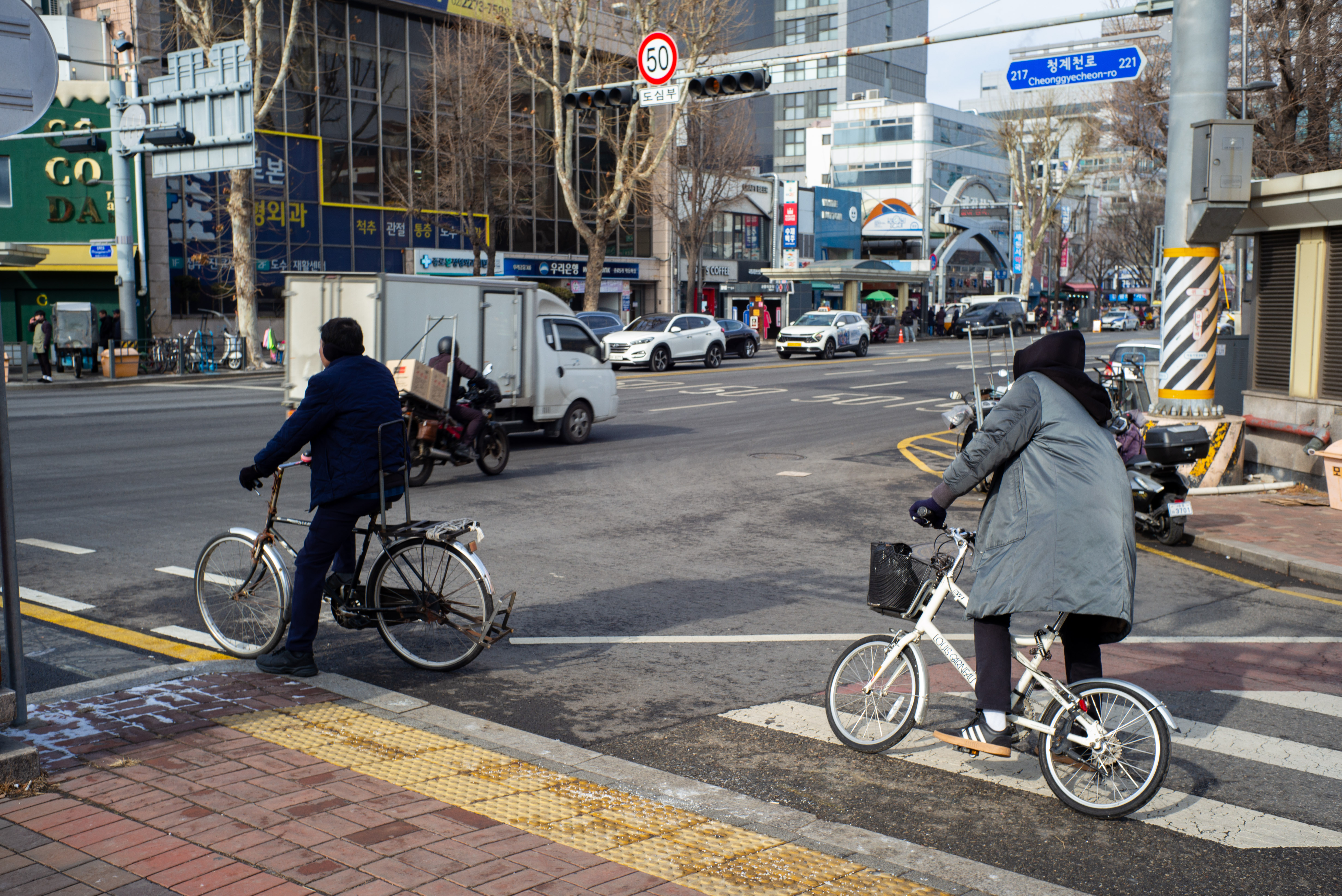 서울 청계천로 표지판이 보이는 교차로에서 자전거를 타고 횡단보도를 건너는 사람들의 일상 풍경