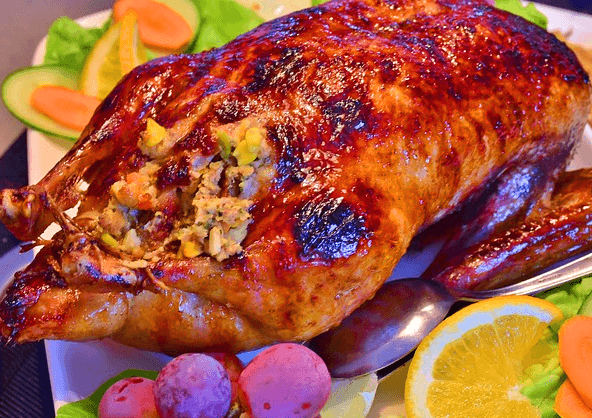 하얀 접시에 노릇하게 잘 구운 오리통구이 한 마리가 있다. 주변에 거봉, 당근, 레몬이 있다.