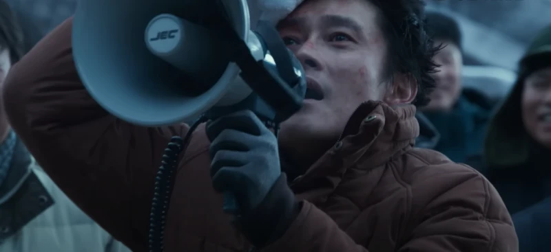 겨울철 장갑을 낀 손으로 한손은 메가폰으로 외치면서 한손은 피가나는 머리를 지혈하고 있는 이병헌