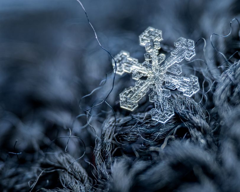 Macro shot of fragile snowflake placed on warm black fabric of wool with separate filaments