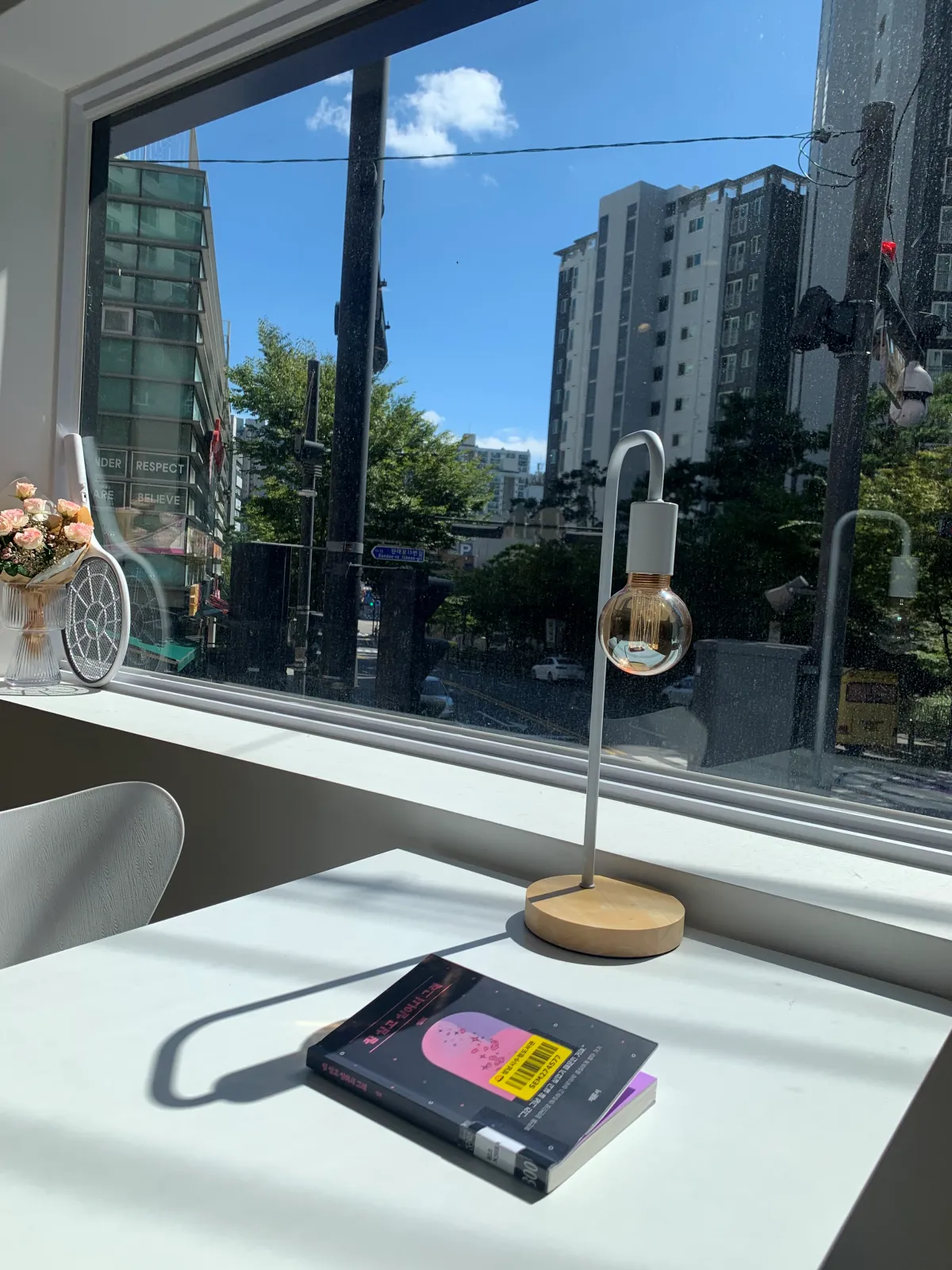 통창옆-흰색테이블위에-책한권과-스탠드조명이-놓여있다