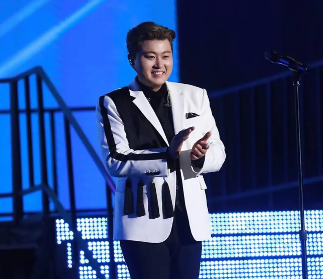 파란배경 흰 쟈켓을 입은 김호중이 웃으며 박수치는 모습