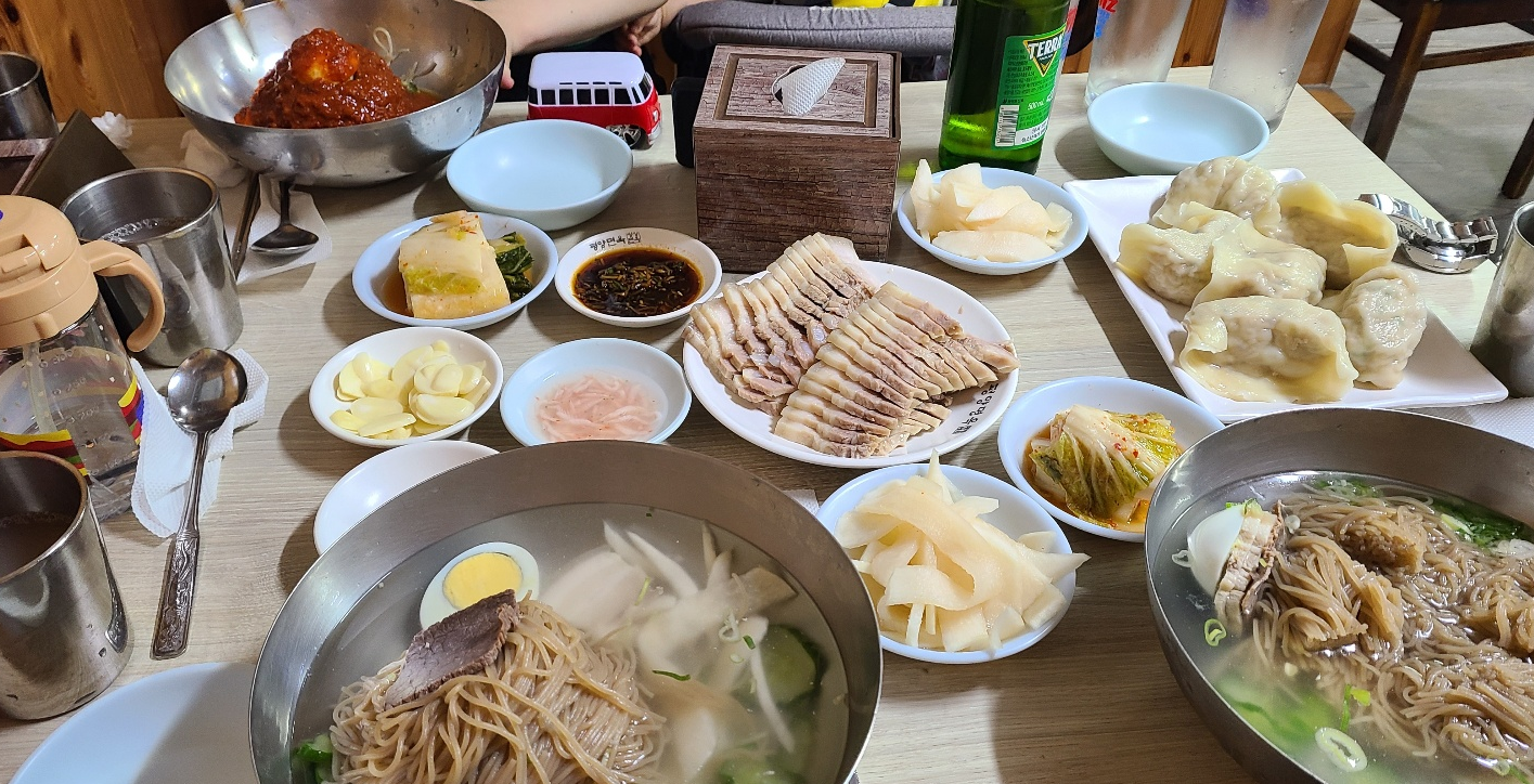 테이블에 수육과 만두 그리고 물냉면과 비빔냉면이 있다.