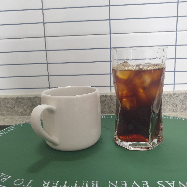 초록색 매트 위에 자기컵과 유리컵이 있다. 각각 핫 커피와 아이스 커피가 담겨있다.