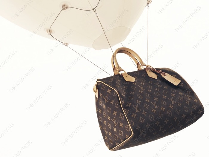 ⁠Louis Vuitton monogram bag suspended by a white balloon floating in the air to showcase lightweight tech⁠