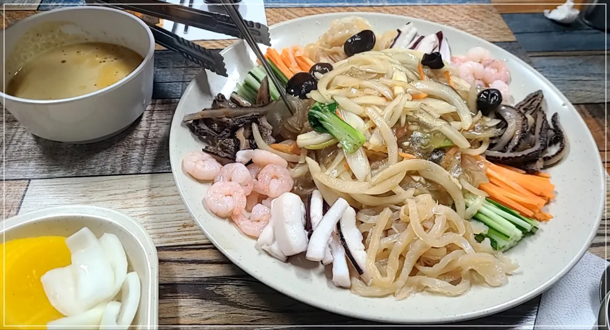 나무테이블 위 흰접시에 담긴 양장피, 흰그릇에 겨자소스와, 흰접시에 단무지 양파가 담겨있음