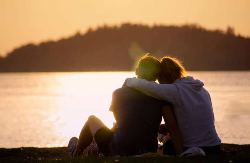 호수 앞에서 노을을 바라보며 서로에게 기대어 앉아 있는 중년 부부의 모습. 갱년기 여성의 정서적 안정을 상징