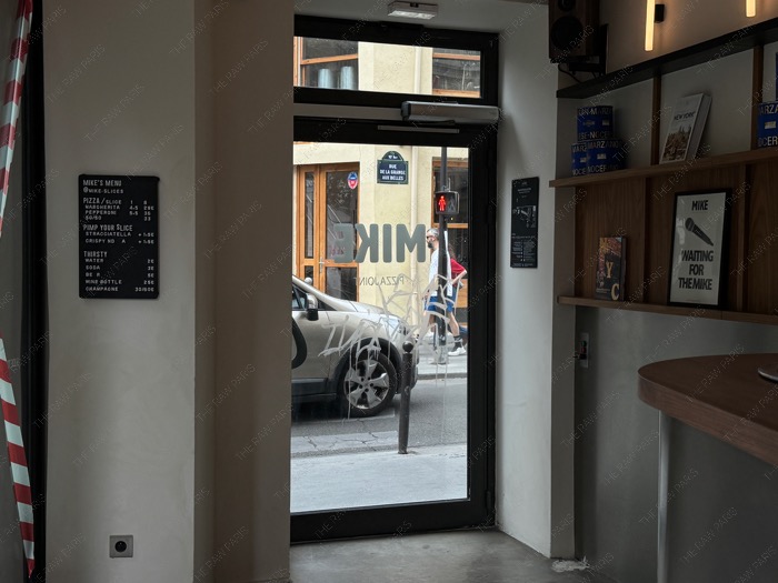 Second View from inside MIKE pizza shop looking out a large open window onto a Paris street crossing near the canal