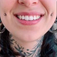 목에-문신을하고-볼-양쪽에-피어싱을하며-미소를-띠며-가지런히-정돈된-하얀이를-드러내는-여인