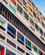 르 코르뷔지에가 설계한 유니테 다비타시옹의 옥상 풍경. 조각처럼 생긴 환기탑과 곡선 형태의 구조물이 흰색 콘크리트로 구성되어 있으며, 주변에는 트랙과 놀이 공간이 펼쳐져 있다. 배경으로는 푸른 하늘과 도시 풍경이 어우러짐.&rdquo;