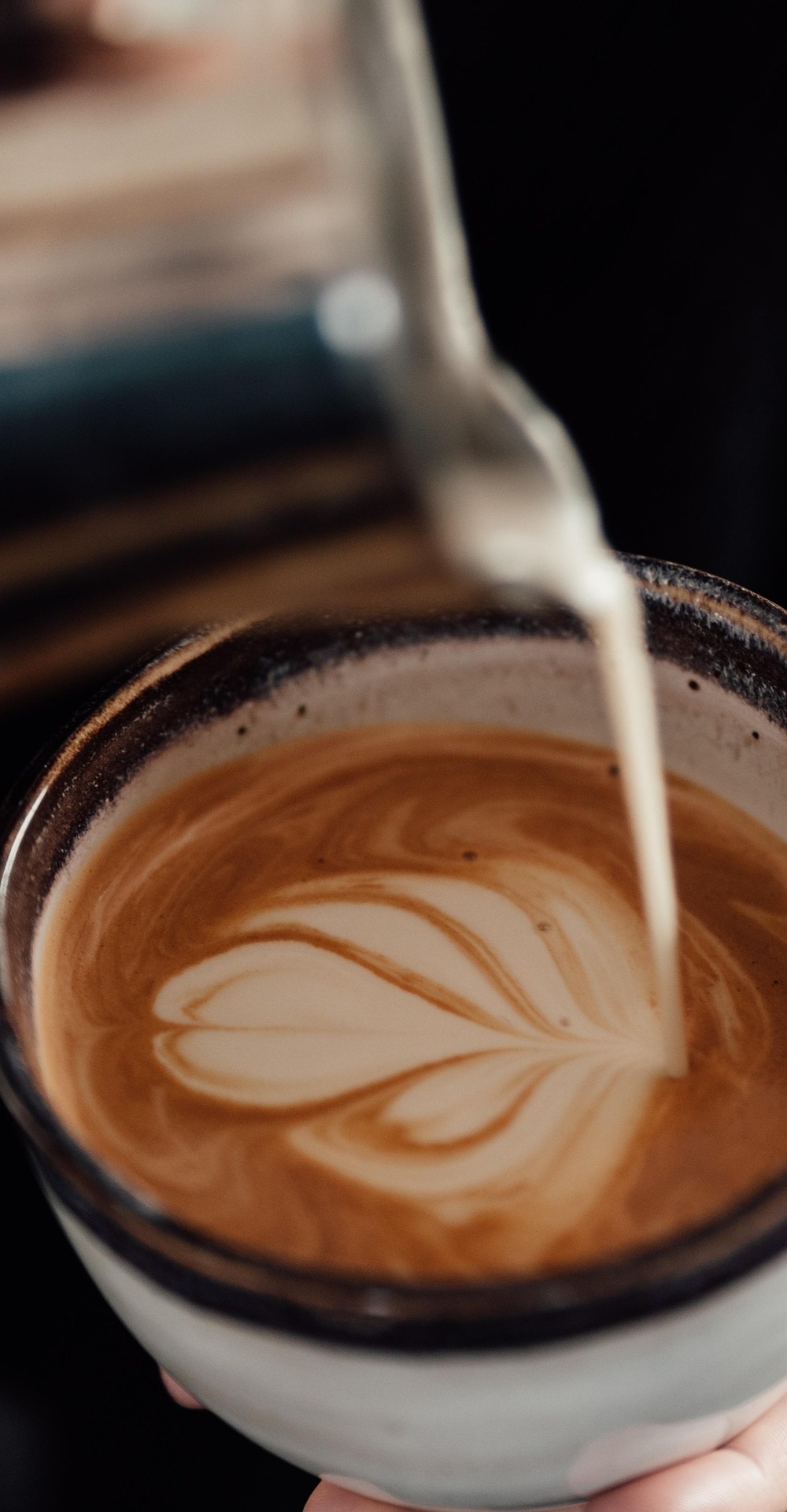 따뜻한 세라믹 컵에 우유를 부어 하트 모양 라떼 아트를 만들고 있는 모습